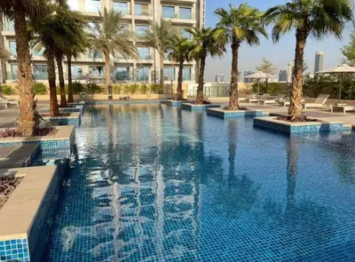 a large swimming pool with palm trees and a building at Ghalia Studio Apartment in Dubai