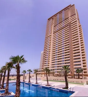 a large building with palm trees in front of a pool at Ghalia Studio Apartment in Dubai