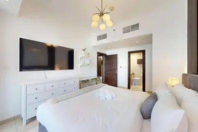a white bedroom with a large white bed and a tv at Silverene Tower B - Exciting Two Bedroom in Dubai