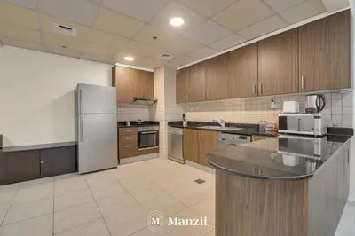 a large kitchen with wooden cabinets and a refrigerator at Manzil - 1BR in Elite Residence with Marina View in Dubai