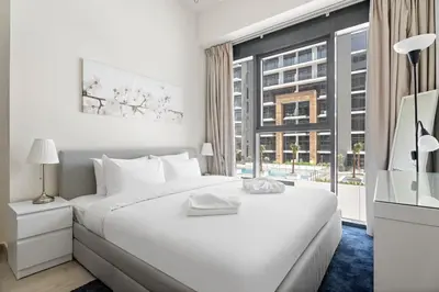 a white bedroom with a large bed and a window at Beautiful 1 BR with Gym, Pool & Kid's Playground in Dubai