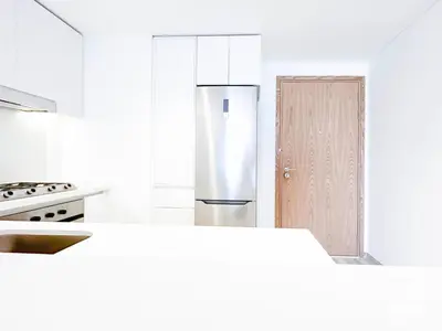 a white kitchen with a refrigerator and a door at Modern 1-Bedroom Haven in Ahad Residence in Dubai