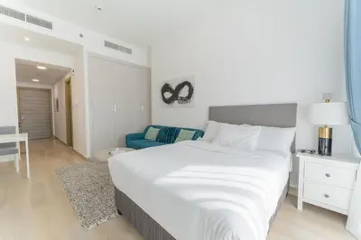 a bedroom with a large white bed and a blue couch at HAVN - Studio Apartment in Bloom Towers, JVC in Dubai