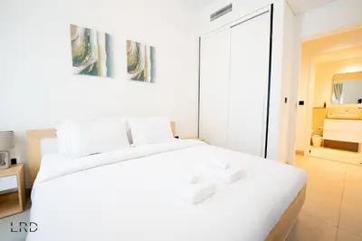 a white bedroom with a white bed and a mirror at New Cozy 1BR Dubai Hills in Dubai