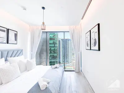 a white bedroom with a bed and a large window at Stylish 1Bedroom with Balcony & View Dubai in Dubai