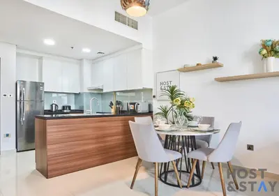 a kitchen with a table with chairs and a refrigerator at Serene 1 BR in Damac Hills - Host & Stay in Dubai