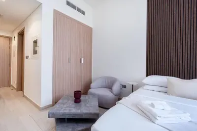 a white bedroom with a bed and a chair at 12 min from downtown - Studio - Azizi Riviera in Dubai