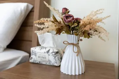 a vase with flowers on a table next to a bed at 1 bedroom - 12 min from downtown - Azizi Riviera in Dubai