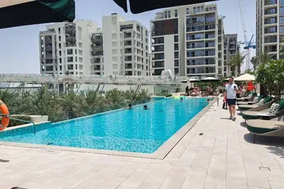 a man standing next to a swimming pool with buildings at New Listing & Vida Creek Beach & Beach Access in Dubai