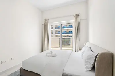 a white bedroom with a bed and a window at Modern 1 bedroom apartment in Sports City in Dubai