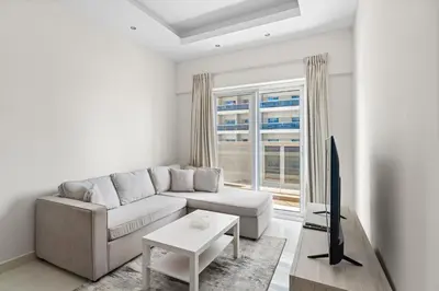 a white living room with a couch and a tv at Modern 1 bedroom apartment in Sports City in Dubai