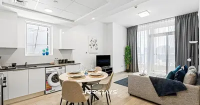 a kitchen and living room with a table and a couch at Stunning Luxury 1BR - Modern with Pool View - JVC in Dubai