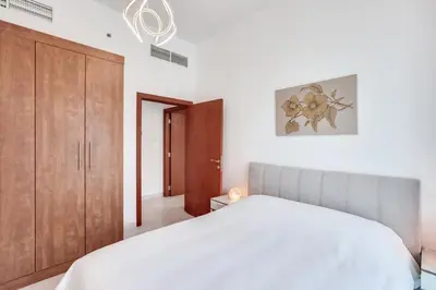 a bedroom with a white bed and a wooden cabinet at Stylish 2bd with great view in Marina View Tower in Dubai