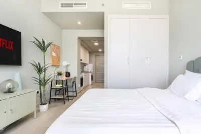a bedroom with a large white bed and a kitchen at Cosy Studio Apartment in Bloom Towers, Jumeirah Village Circle in Dubai