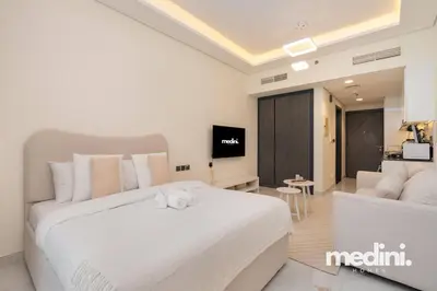 a bedroom with a large white bed and a living room at Studio in Samana Golf Avenue - Dubai in Dubai