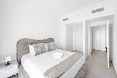 a white bedroom with a large white bed and a table at Elegant - 1BR - 8 MIN Burj Khalifa & Dubai Mall in Dubai