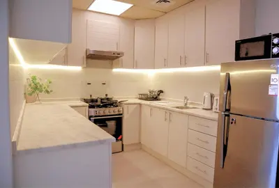 a kitchen with white cabinets and a stainless steel refrigerator at Spacious 1BR, Pool, Gym, Near Dining & Shops in Dubai