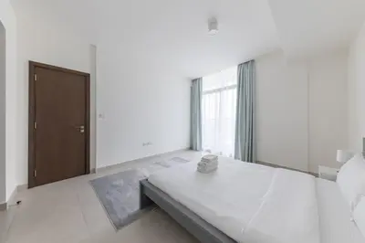 a white bedroom with a bed and a wooden door at Splendid 1BR in Living Garden in Dubai