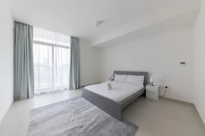 a white bedroom with a bed and a large window at Splendid 1BR in Living Garden in Dubai
