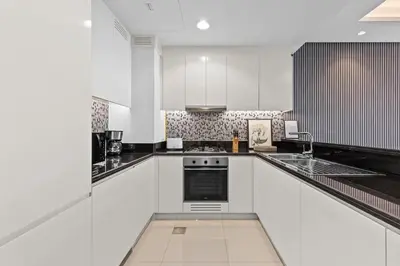 a white kitchen with black and white appliances at Luxury Stay with Burj Khalifa Views & Infinity Pool in Dubai