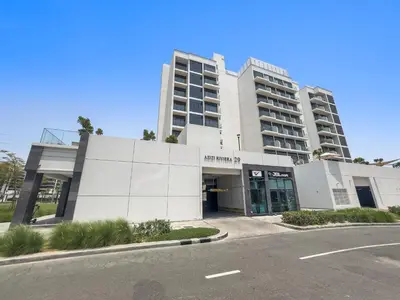 a white building with a parking lot in front of it at Lovely Studio with Gym, Pool and BBQ Facilities in Dubai