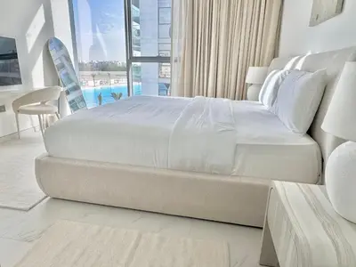 a white bed in a bedroom with a large window at Residences 29 - Divine Beachfront One Bedroom in Dubai