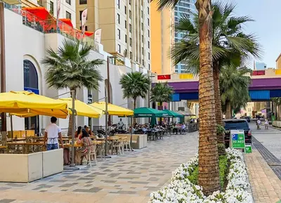 a palm tree on a city street with tables and umbrellas at Best Spot in Marina Dubai in Dubai