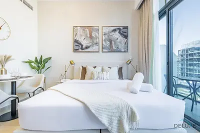a white bedroom with a large bed and a table at Alluring Studio Apartment at Azizi Riviera 16, Al Merkadh by Deluxe Holiday Homes in Dubai