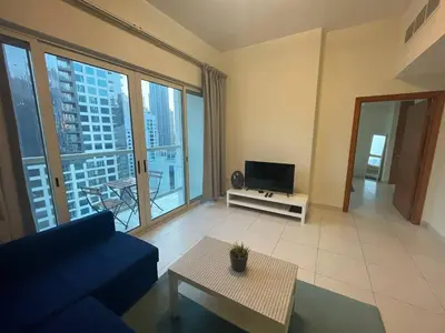 a living room with a blue couch and a tv at Very Convenient Apartment steps to Metro and Marina Mall Managed by SunnyHomes in Dubai