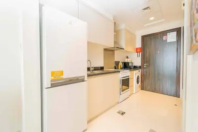 a kitchen with white cabinets and a refrigerator at Golf View Studio in Damac Hills - Luxury Living, Exclusive Amenities, by Think Realty in Dubai