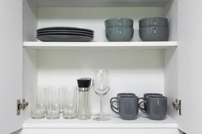 a shelf with dishes and glasses and a wine glass at Chic studio near metro at Discovery Gardens in Dubai