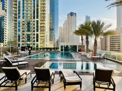 a swimming pool with chairs and palm trees and buildings at Vacation Friendly Beach View Luxury 1Bedroom- Walk To Beach & Mall in Dubai