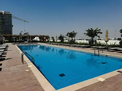 a large blue swimming pool with chairs and a building at Golfville LighthouseDubai Hills in Dubai
