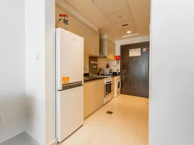 a kitchen with a white refrigerator in a room at Studio in Damac Hills - Modern Comfort with Premium Amenities,by Think Realty in Dubai