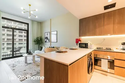 a kitchen with wooden cabinets and a living room at 2ndHome - Laya Heights, Studio City in Dubai