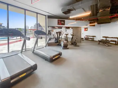 a gym with cardio equipment in a large room with windows at Cozy Studio with sun terrace in Dubai