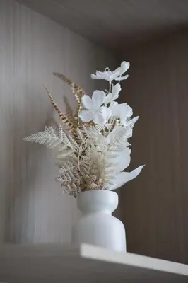 a white vase with flowers in it on a shelf at Cozy Studio in Westwood By IMTIAZ in Dubai