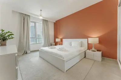 a bedroom with a white bed and an orange wall at Prime Downtown 2BR Retreat in Dubai