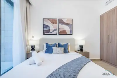 a bedroom with a white bed with blue pillows at Stylish Studio Apartment in Azizi Riviera 37 Al Merkadh by Deluxe Holiday Homes in Dubai