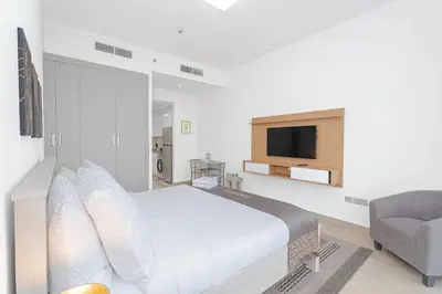 a white bedroom with a bed and a chair at Escape24 Cozy Studio with City View in JVC in Dubai