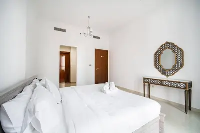 a white bedroom with a bed and a mirror at Elegant Escapes - Homely 1B in Dunya Tower in Dubai