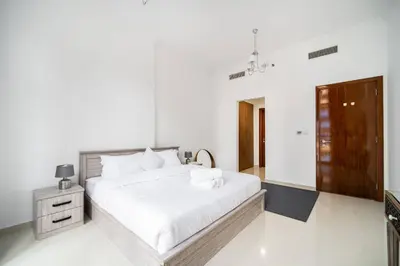 a white bedroom with a large bed and a wooden cabinet at Elegant Escapes - Homely 1B in Dunya Tower in Dubai