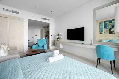 a bedroom with a bed with a television and blue chairs at Goldbest - Seven Palm 4ppl in Dubai