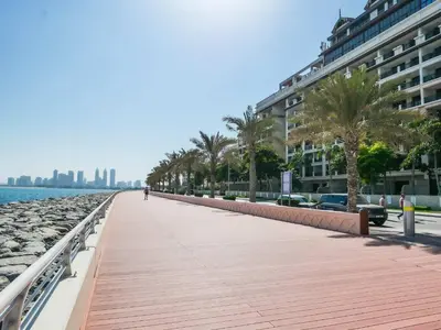a boardwalk on the beach with palm trees and a building at Stunning Renovated 1BR Apartment at 5 Star Resort in Dubai
