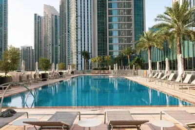 a swimming pool with chairs and palm trees and buildings at PrimeForte Walk to Dubai Mall in Dubai