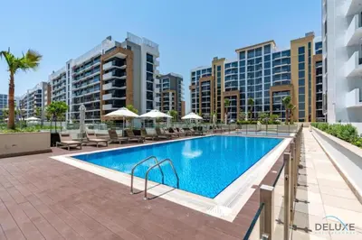 a swimming pool with chairs and umbrellas in front of buildings at Comfortable Studio in Azizi Riviera 24, Al Merkadh by Deluxe Holiday Homes in Dubai