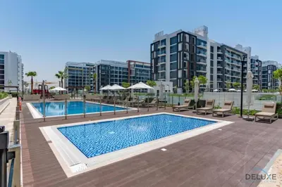 a swimming pool with chairs and buildings in the background at Comfortable Studio in Azizi Riviera 24, Al Merkadh by Deluxe Holiday Homes in Dubai