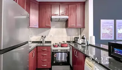 a kitchen with red cabinets and a stove top oven at Rare Holiday Homes - Mediterranean Cluster - Near Ibn Battuta Mall - Discovery Garden - Building# Med 49 - R411 in Dubai