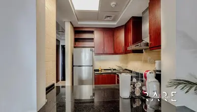 a kitchen with wooden cabinets and a stainless steel refrigerator at Rare Holiday Homes - Mediterranean Cluster - Near Ibn Battuta Mall - Discovery Garden - Building# Med 100 - RG13 in Dubai
