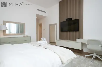 a white bedroom with a bed and a desk and a tv at Mira Holiday Homes - Luxury 2 bedroom in Le Pont in Dubai